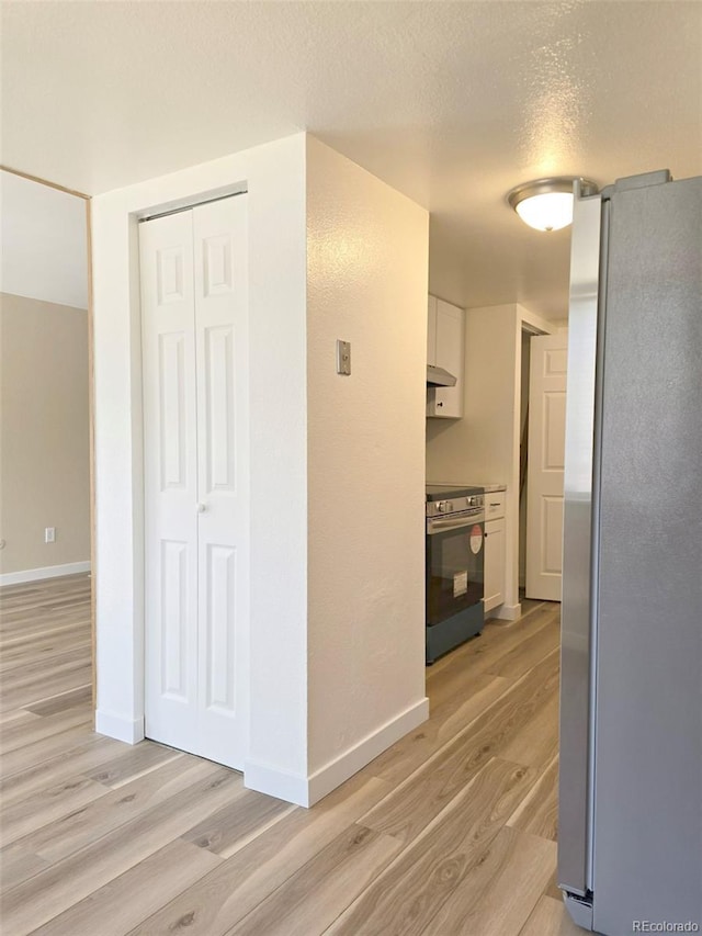 hallway with light wood finished floors, a textured ceiling, and baseboards