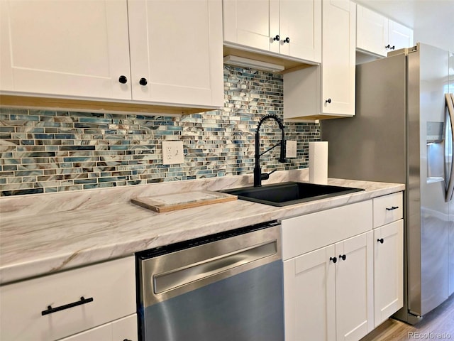 kitchen featuring a sink, backsplash, wood finished floors, white cabinets, and dishwasher