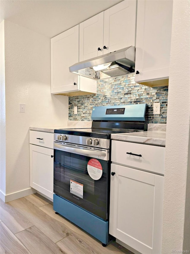 kitchen with under cabinet range hood, backsplash, stainless steel electric stove, and white cabinetry