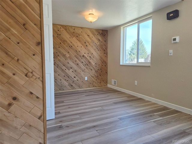 empty room featuring wood finished floors, visible vents, wood walls, and baseboards