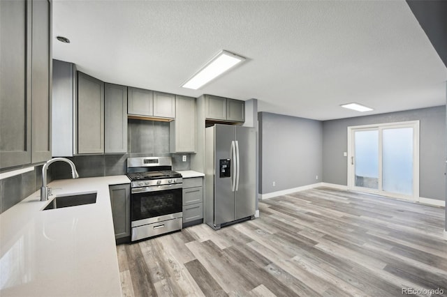 kitchen featuring sink, light hardwood / wood-style flooring, gray cabinets, a textured ceiling, and appliances with stainless steel finishes