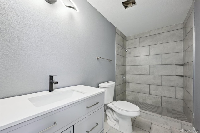 bathroom featuring tile patterned flooring, vanity, toilet, and tiled shower