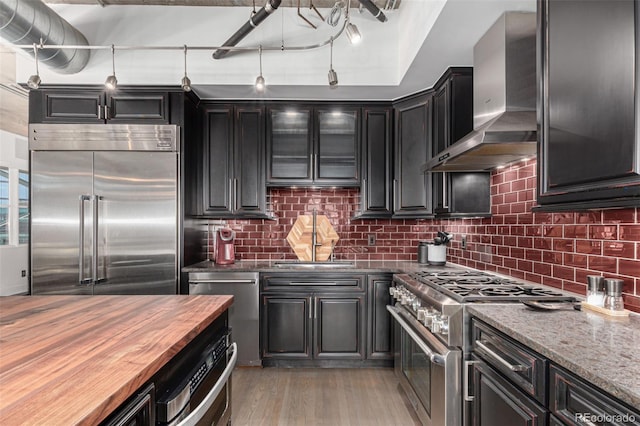 1735 19th St Unit 6D, Denver, CO 80202 - kitchen with high end appliances, wall chimney exhaust hood, wooden counters, light wood-style floors, and decorative backsplash