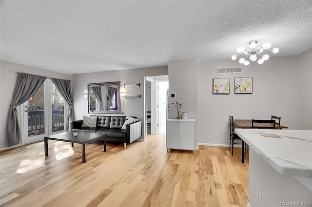 interior space featuring a chandelier, a textured ceiling, light wood-style flooring, visible vents, and baseboards