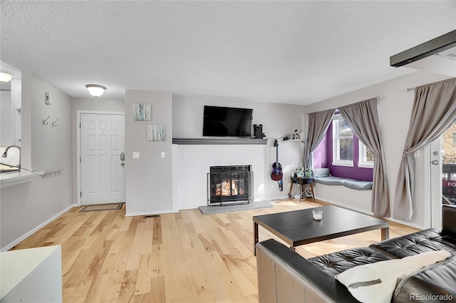 living area with a textured ceiling, wood finished floors, a glass covered fireplace, and baseboards