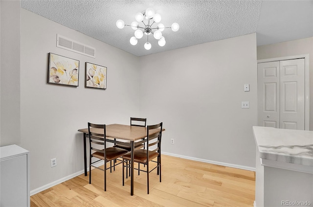 dining area featuring a textured ceiling, light wood-style flooring, a notable chandelier, visible vents, and baseboards