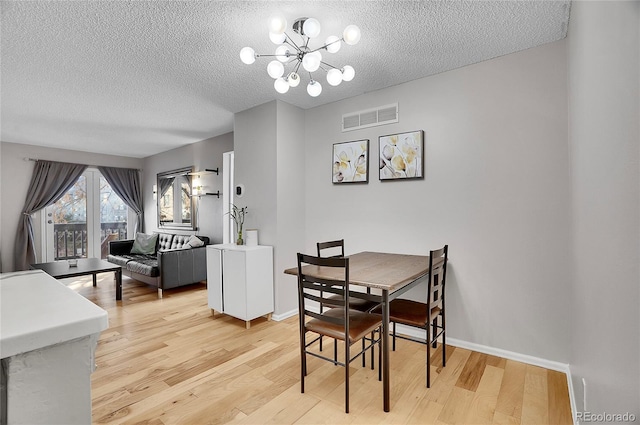 dining area featuring a notable chandelier, light wood finished floors, visible vents, a textured ceiling, and baseboards