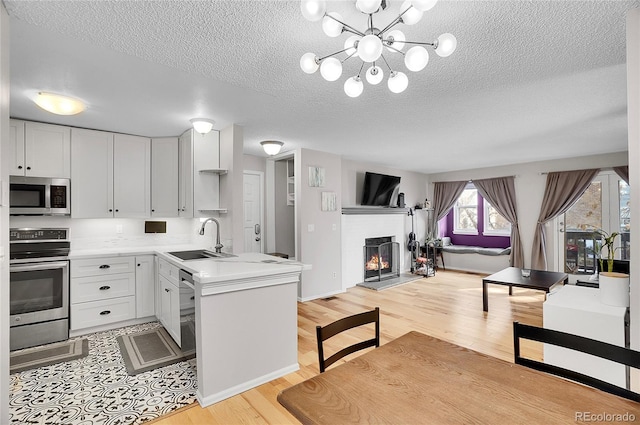 kitchen with white cabinets, open floor plan, stainless steel appliances, light countertops, and a sink