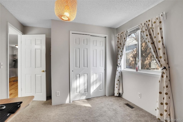 unfurnished bedroom featuring carpet, a textured ceiling, visible vents, and a closet