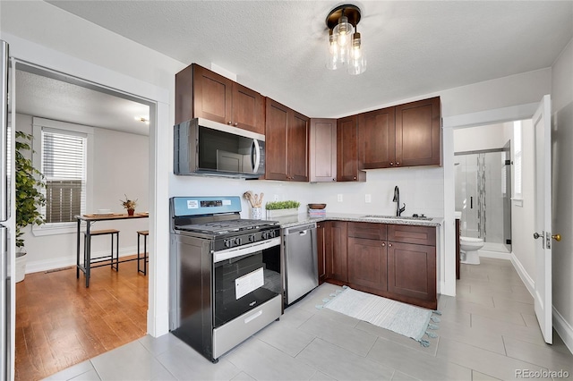 kitchen featuring a sink, stainless steel appliances, baseboards, and a textured ceiling