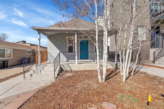 view of front facade featuring a shingled roof, a porch, and stucco siding