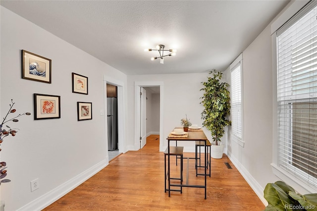 dining space with baseboards, visible vents, light wood finished floors, a textured ceiling, and a notable chandelier