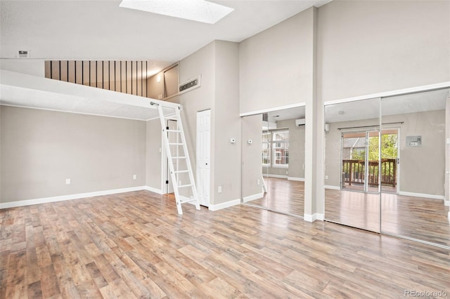 unfurnished living room with a skylight, high vaulted ceiling, wood finished floors, and baseboards