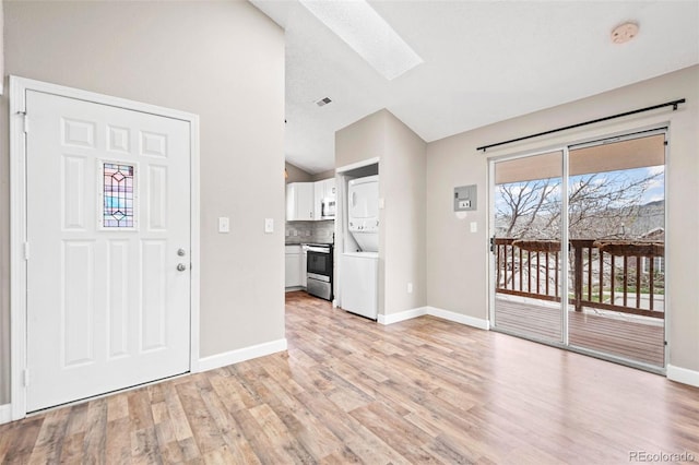 entryway featuring stacked washer / drying machine, a skylight, lofted ceiling, light wood-style floors, and baseboards