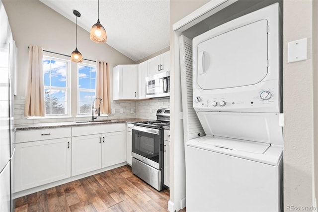 kitchen featuring stainless steel appliances, stacked washer and clothes dryer, a sink, lofted ceiling, and white cabinets