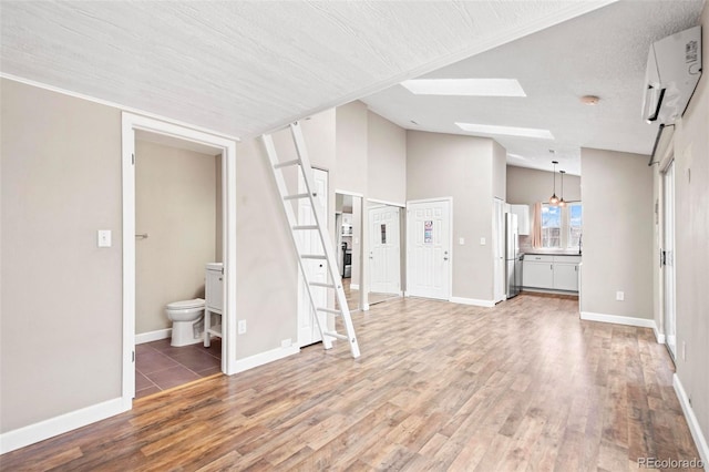 unfurnished living room featuring light wood finished floors, a skylight, a wall mounted AC, baseboards, and high vaulted ceiling