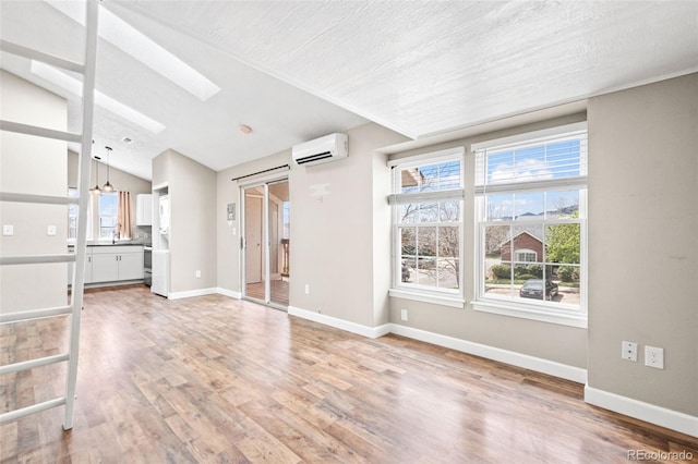 unfurnished living room with a wall mounted AC, a skylight, vaulted ceiling, and light wood-type flooring
