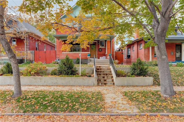 view of front of home featuring brick siding, stairway, a porch, and fence