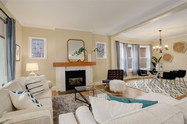 living room with wood finished floors, a brick fireplace, crown molding, and an inviting chandelier