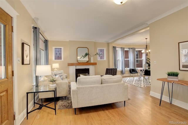 living room featuring baseboards, wood finished floors, crown molding, a fireplace, and a notable chandelier