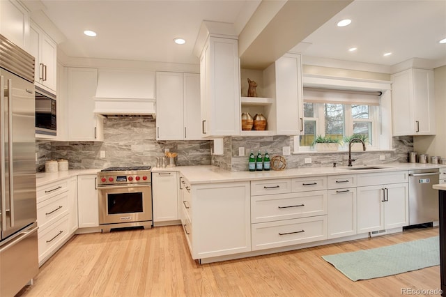 kitchen with custom range hood, built in appliances, white cabinetry, open shelves, and a sink