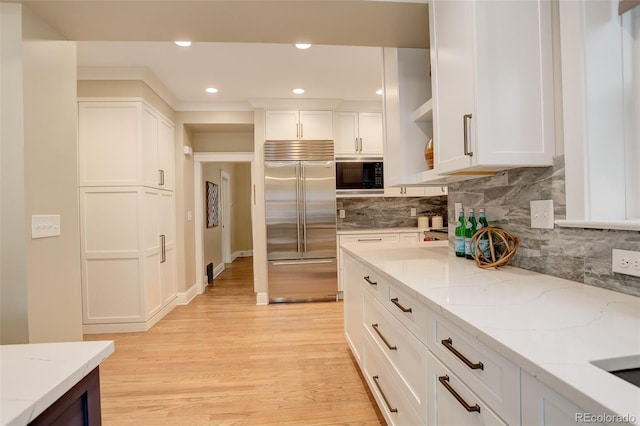 kitchen with light stone counters, white cabinetry, light wood-style flooring, and built in appliances