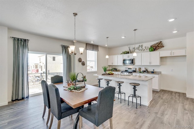 dining space with sink, a chandelier, a textured ceiling, and light wood-type flooring