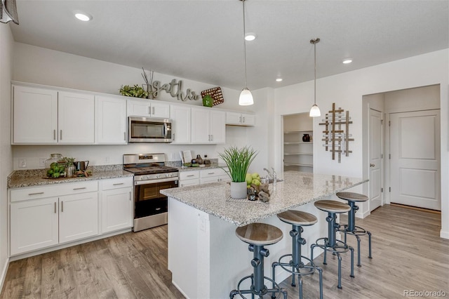 kitchen with stainless steel appliances, an island with sink, pendant lighting, white cabinets, and light wood-type flooring