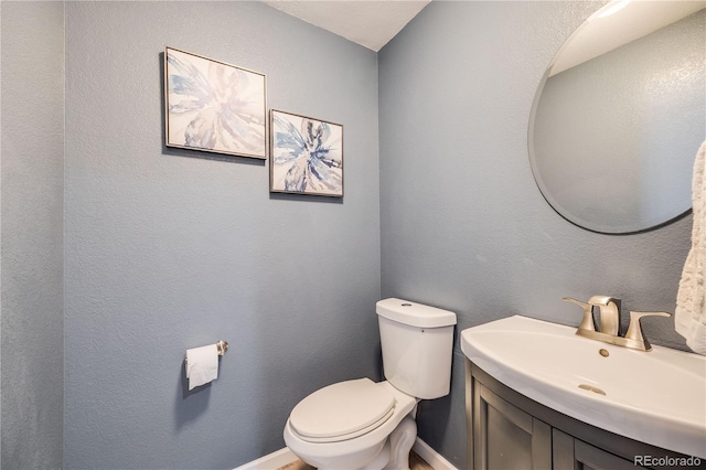 half bathroom featuring toilet, vanity, and baseboards