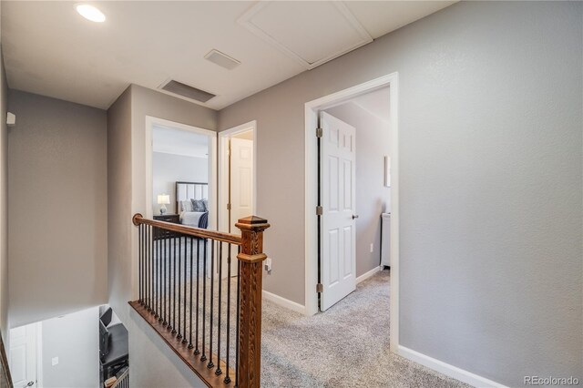 hallway featuring baseboards, visible vents, light colored carpet, and an upstairs landing