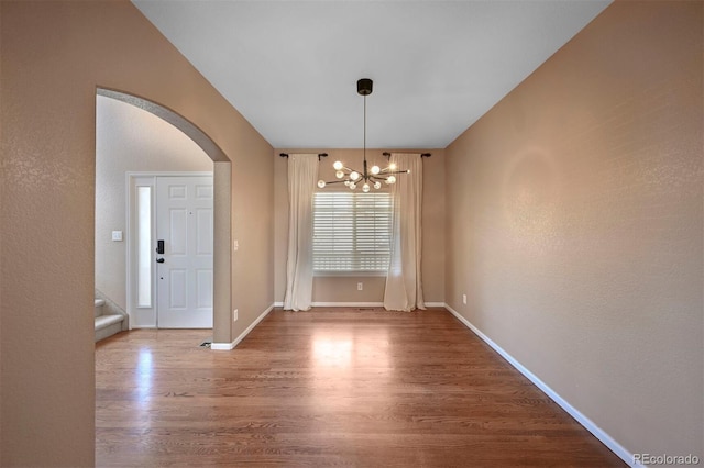 unfurnished dining area featuring arched walkways, wood finished floors, stairs, a notable chandelier, and baseboards