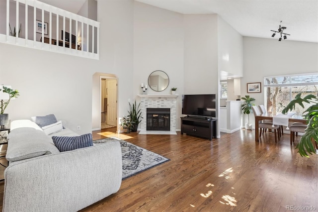 living area with baseboards, a tile fireplace, wood finished floors, arched walkways, and high vaulted ceiling