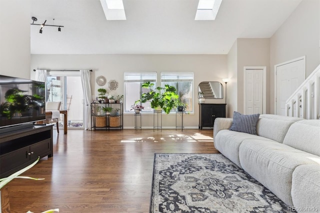 living room featuring lofted ceiling with skylight, plenty of natural light, wood finished floors, and baseboards