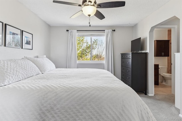 bedroom featuring ensuite bath, arched walkways, ceiling fan, a textured ceiling, and light colored carpet