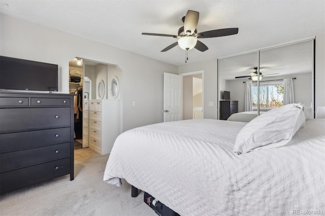 bedroom featuring a closet, light carpet, a walk in closet, and a ceiling fan