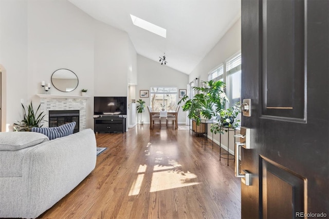 living room featuring a fireplace, a skylight, wood finished floors, and high vaulted ceiling