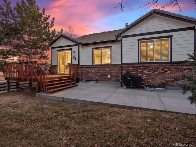 rear view of property featuring a patio area, brick siding, and a wooden deck