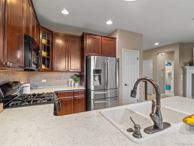 kitchen featuring a fireplace, light countertops, glass insert cabinets, a sink, and black appliances