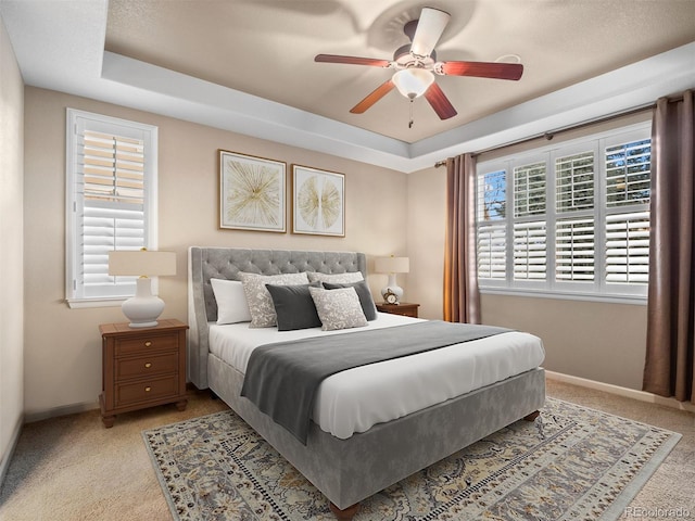 bedroom featuring a tray ceiling, light colored carpet, and baseboards