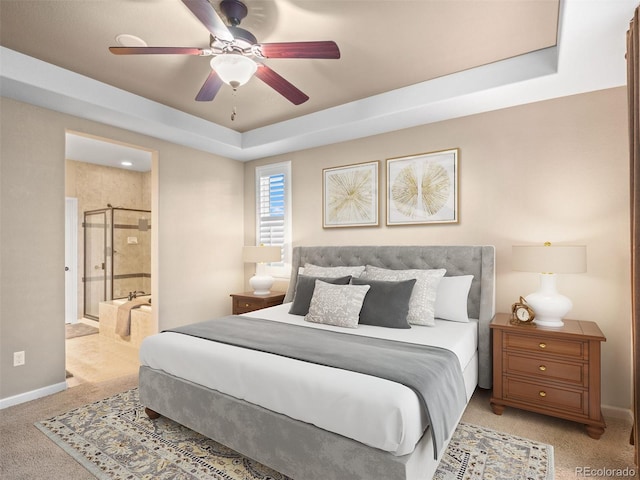 bedroom featuring baseboards, a ceiling fan, light colored carpet, ensuite bathroom, and a tray ceiling