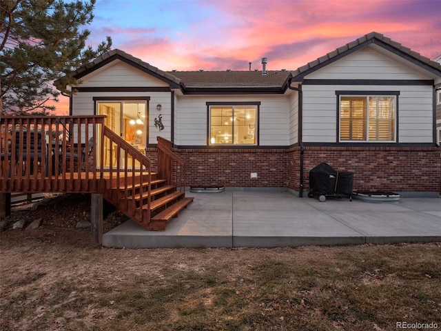 back of house at dusk featuring a patio and brick siding