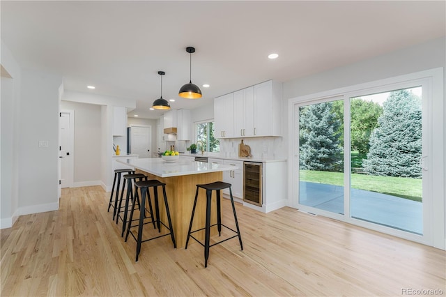 kitchen with light hardwood / wood-style flooring, wine cooler, white cabinets, a kitchen island, and decorative light fixtures