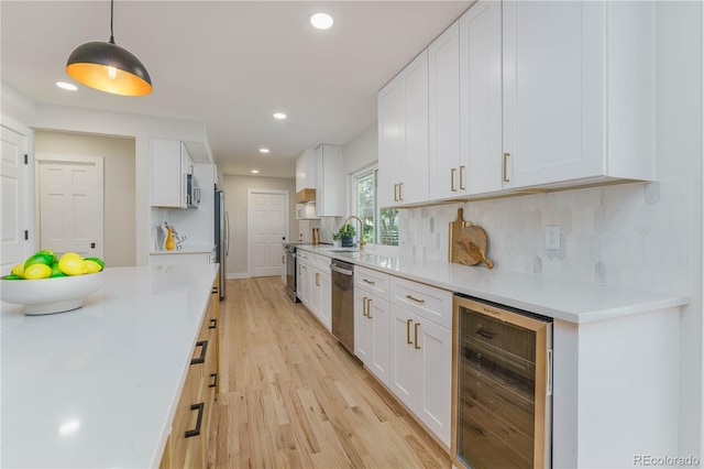 kitchen featuring pendant lighting, appliances with stainless steel finishes, beverage cooler, and white cabinets