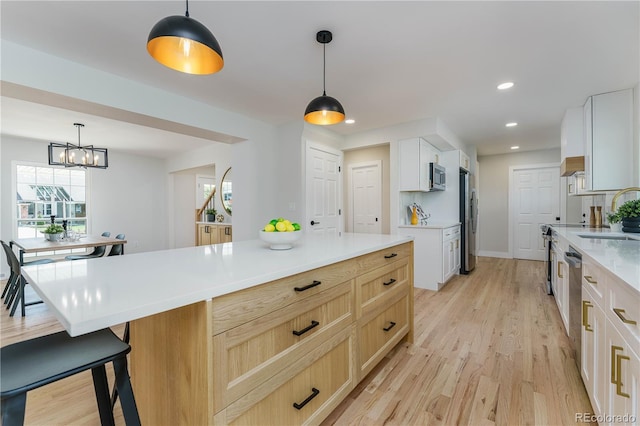 kitchen featuring light brown cabinetry, white cabinetry, decorative light fixtures, and appliances with stainless steel finishes