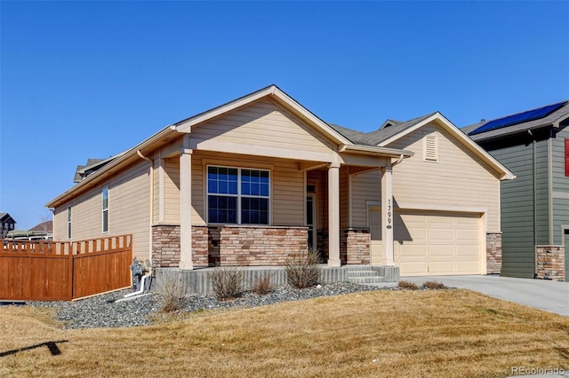 view of front of property with a front lawn, fence, covered porch, stone siding, and driveway