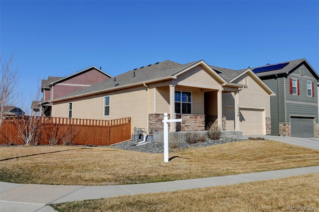 view of front facade featuring stone siding, fence, covered porch, a front yard, and an attached garage