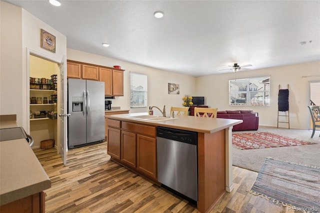 kitchen with a sink, open floor plan, appliances with stainless steel finishes, brown cabinetry, and light countertops