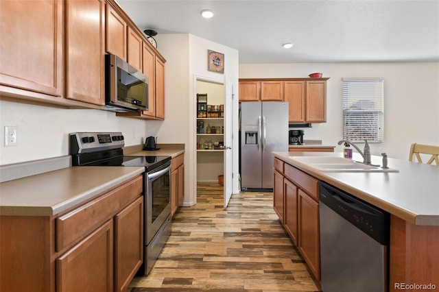 kitchen featuring a sink, recessed lighting, stainless steel appliances, brown cabinetry, and light wood finished floors