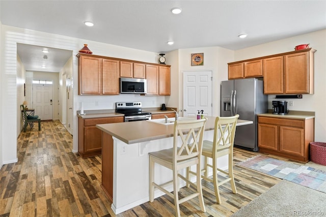 kitchen featuring a breakfast bar area, wood finished floors, a kitchen island with sink, and stainless steel appliances