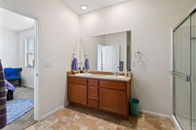 bathroom with a sink, a shower with shower door, double vanity, and stone finish floor